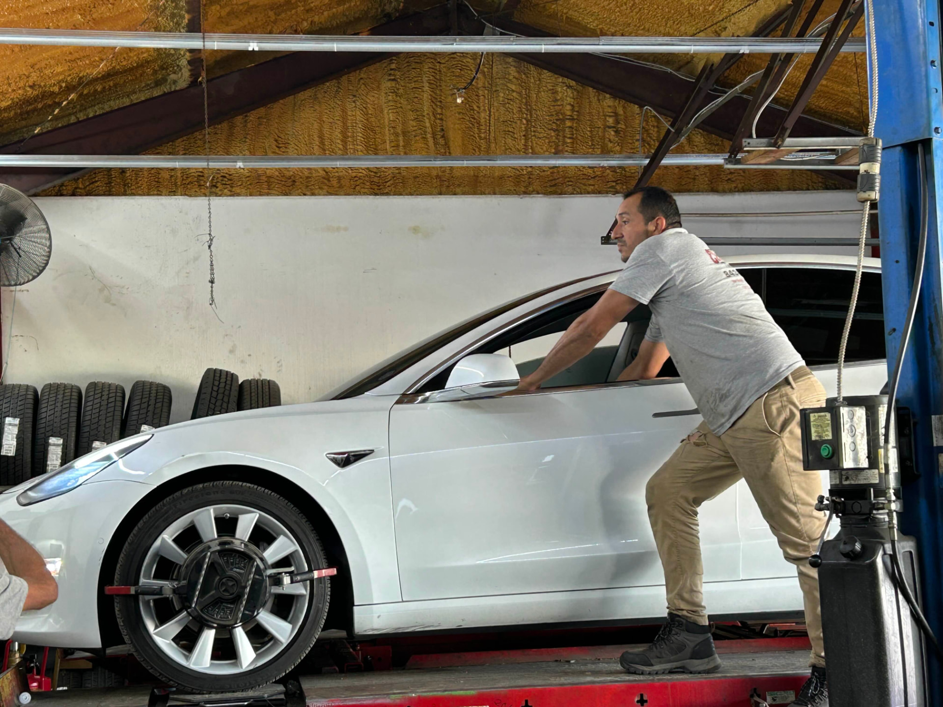 Champion technician performing a wheel alignment on a white Tesla Model 3 at the Rivers Avenue shop