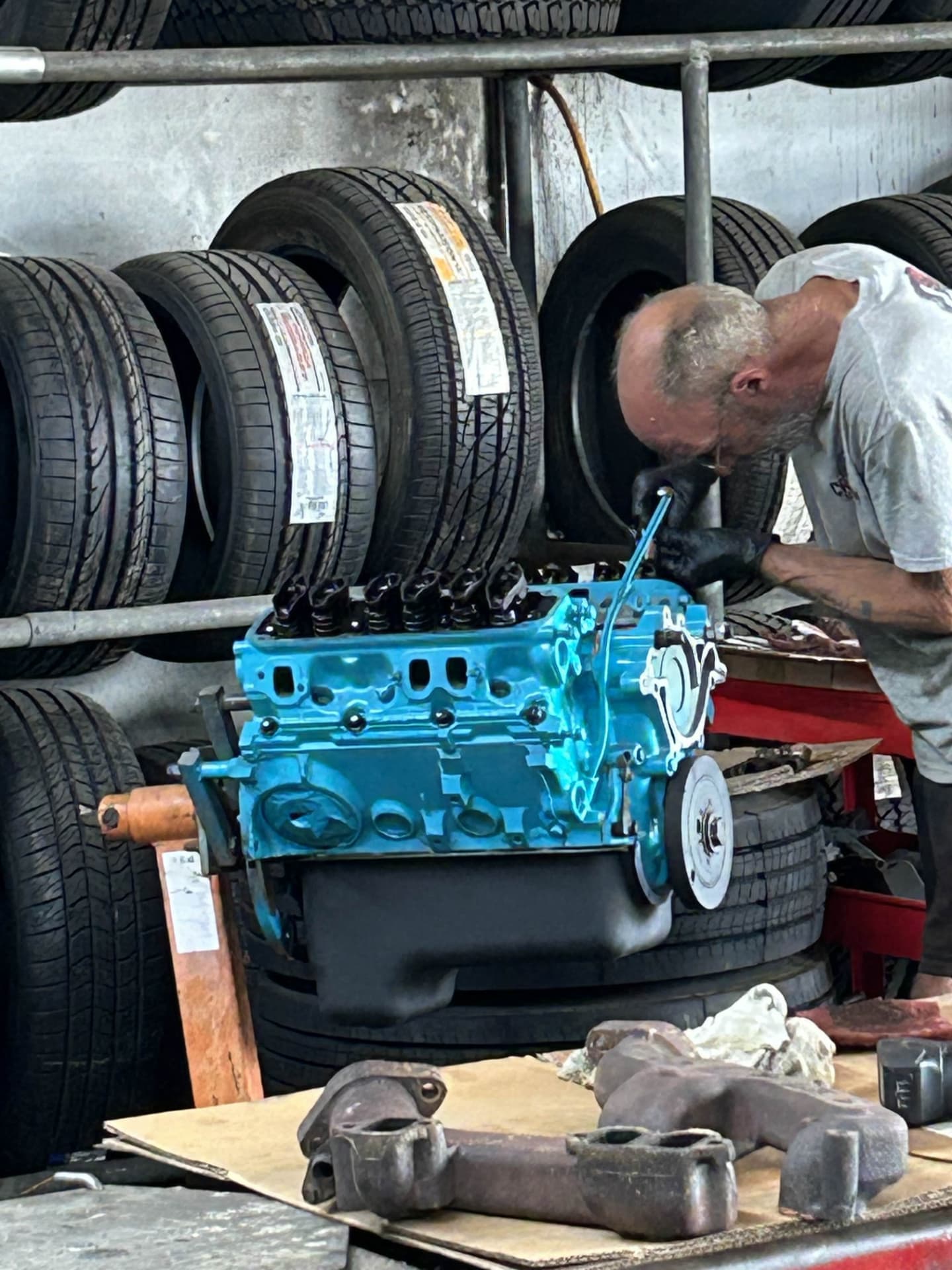 Champion mechanic rebuilding a freshly painted V8 engine block in front of the tire racks in North Charleston
