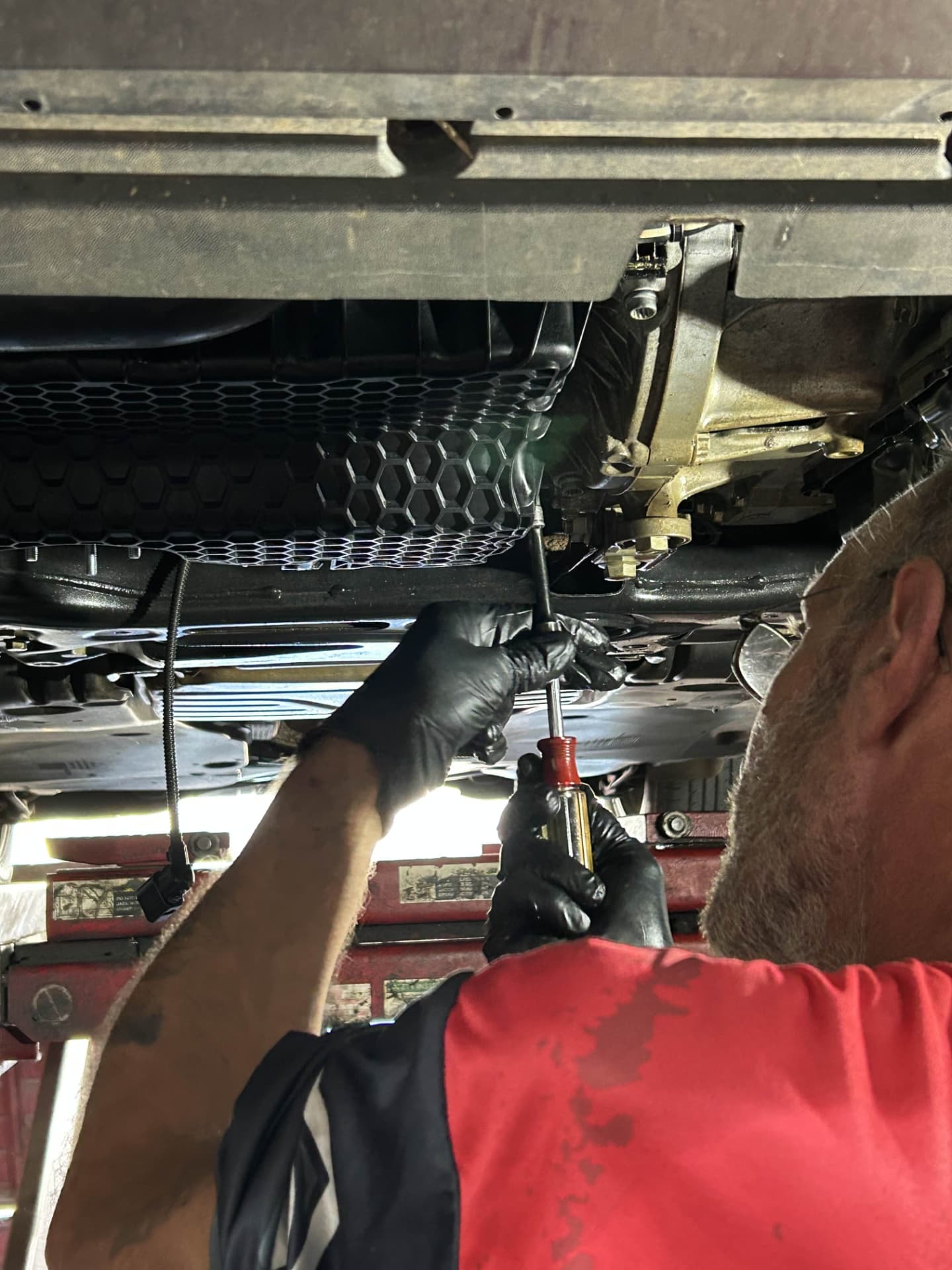 Mechanic draining the oil pan from underneath a vehicle on the lift